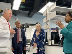 Three people in business attire and a man in a lab coat converse in a lab.