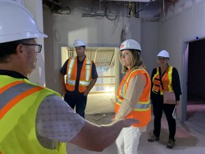 Four people in hard hats and high-visibility vests tour a building that is under renovation.