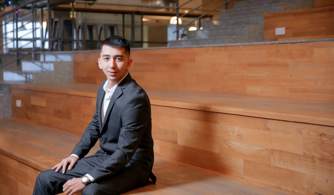 A man in a business suit sits on a wooden stair seating.