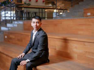 A man in a business suit sits on a wooden stair seating.