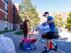 A man carries a full container towards a dolly outside of Brock University’s Vallee Residence.