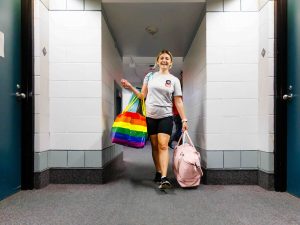 A woman walks down a hallway in Brock University’s Valee Residence while carrying a rainbow coloured bag and pink luggage.