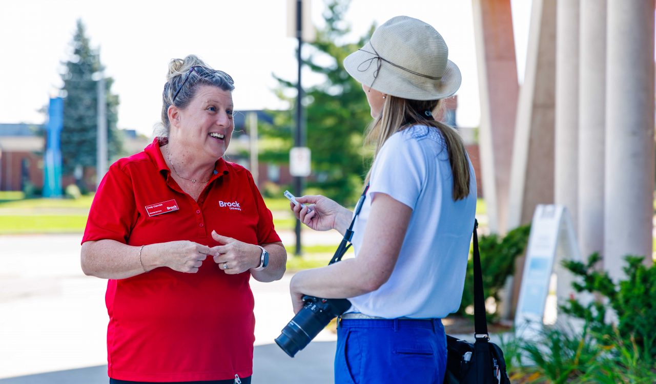 Cindy Chernish wears a red shirt and is interviewed by a St. Catharines Standard reporter at Brock University.