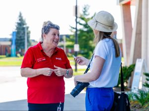 Cindy Chernish wears a red shirt and is interviewed by a St. Catharines Standard reporter at Brock University.