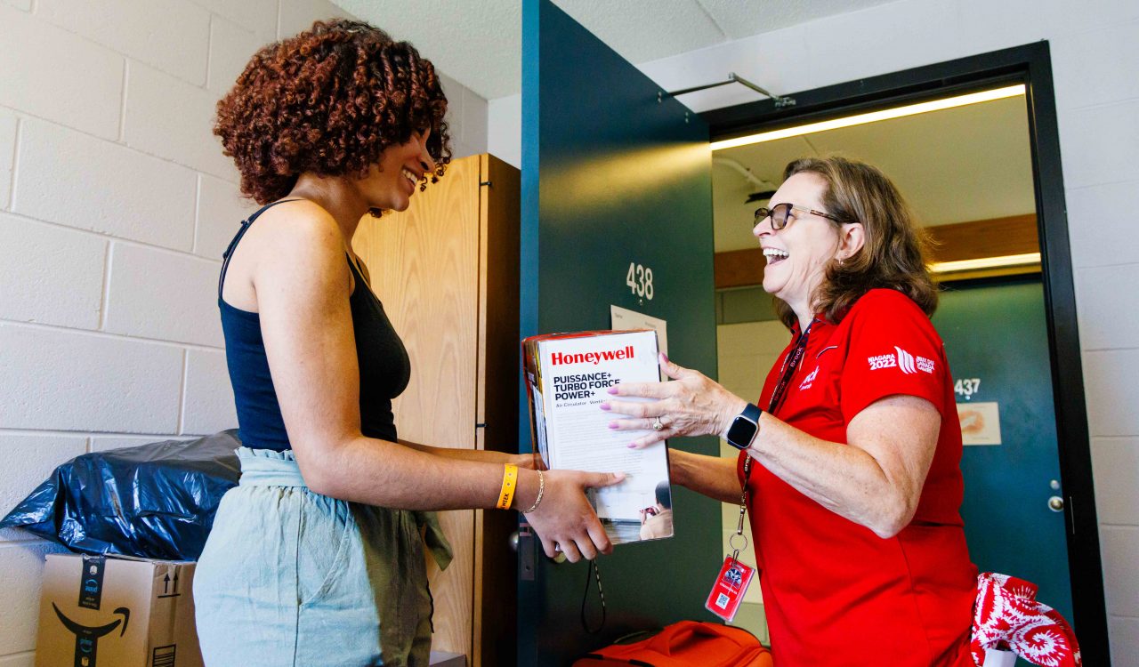 Two women stand looking at one another holding a box between them.