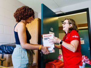 Two women stand looking at one another holding a box between them.