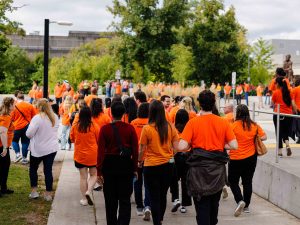 A crowd of people wearing orange shirts stands outside.