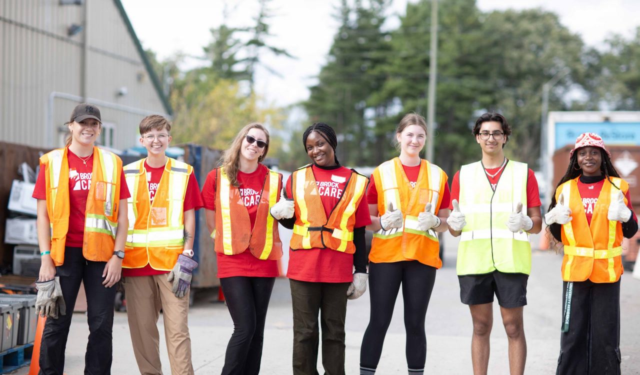 A row of university students poses for a photo while wearing high-visibility vests during a volunteering activity.