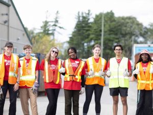 A row of university students poses for a photo while wearing high-visibility vests during a volunteering activity.