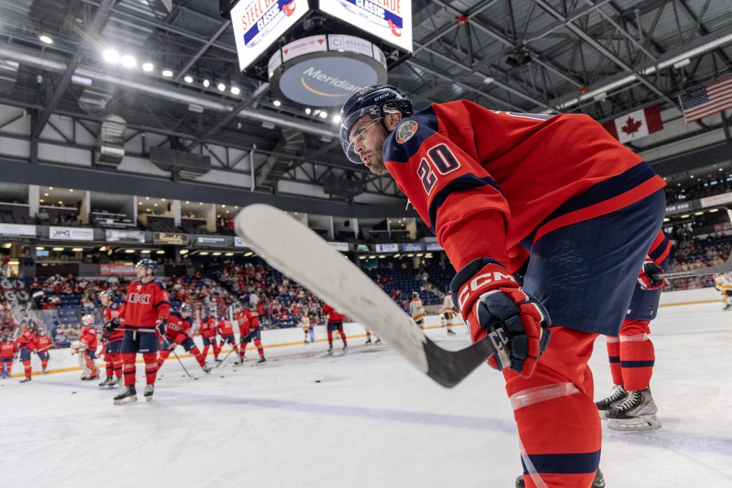 A hockey player stands with his stick off the ice with his teammates are in the background.