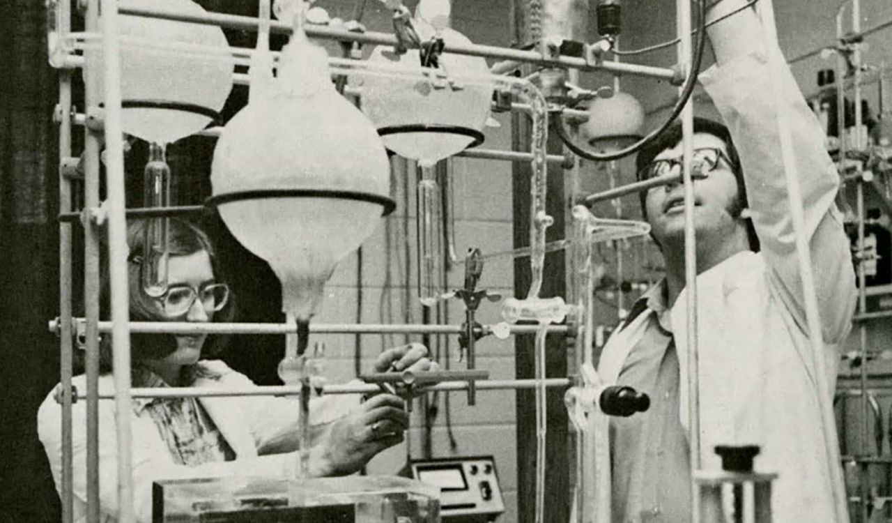 Two scientists, a woman and a man, work in a lab filled with beakers and other equipment.