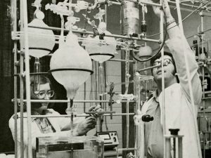 Two scientists, a woman and a man, work in a lab filled with beakers and other equipment.