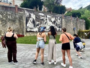 Seen from behind, a group of students look at a monotone grey mural taking photos.