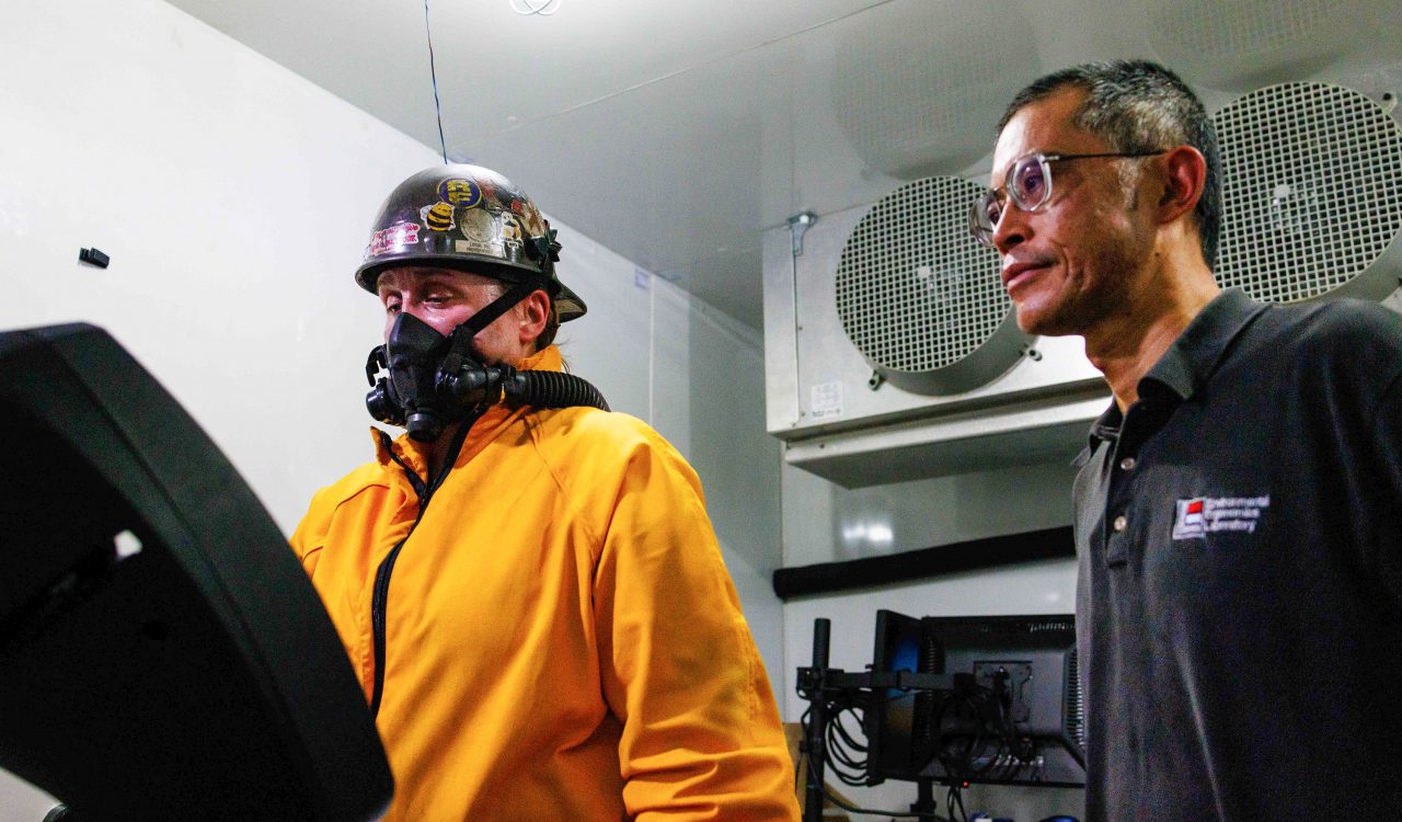 A man looks on while a woman wears protective gear and walks on a treadmill for a scientific experiment,