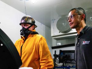 A man looks on while a woman wears protective gear and walks on a treadmill for a scientific experiment,