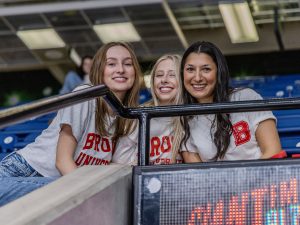 Three women sit in the stands of an arena.