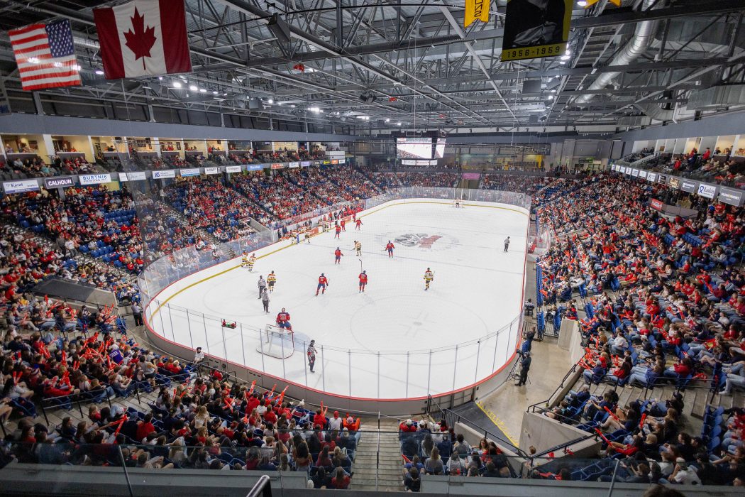 A packed hockey arena with players on the ice.