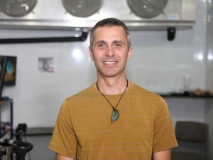 Head-and-shoulders photo of Canada Research Chair Toby Mündel smiling into the camera, with his lab machines blurred out in the background.