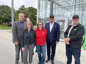 Five people pose for a photo in front of a glass building.