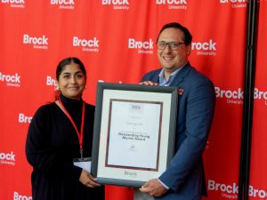 A man and a woman pose for a photo holding a framed certificate between them.