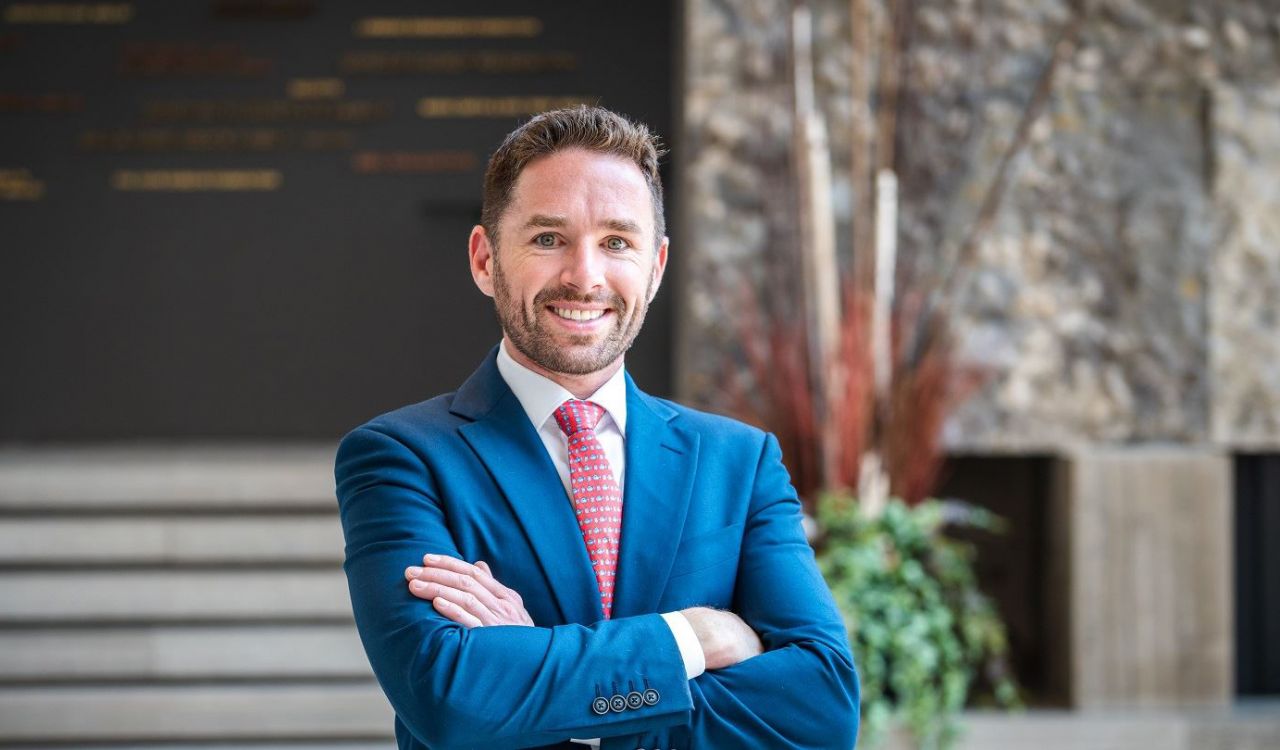 A man in a business suit poses for a photo in front of a building.