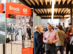 Archival imagery of Brock University is pictured in an indoor space filled with people.