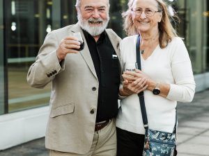 Two people stand together raising their wine glasses outside.