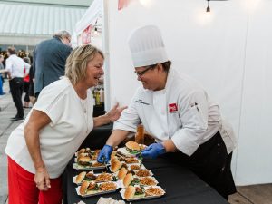 A woman leans in while speaking to a chef who is plating food at an event.