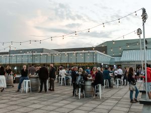 Dozens of people sit around outdoor tables with string lights strung above their heads.