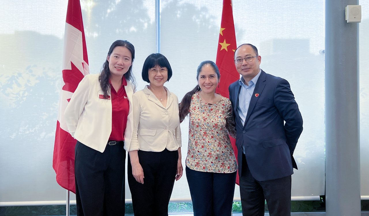 Four people stand together for a photo in front of the Canadian and Chinese flags.