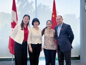 Four people stand together for a photo in front of the Canadian and Chinese flags.