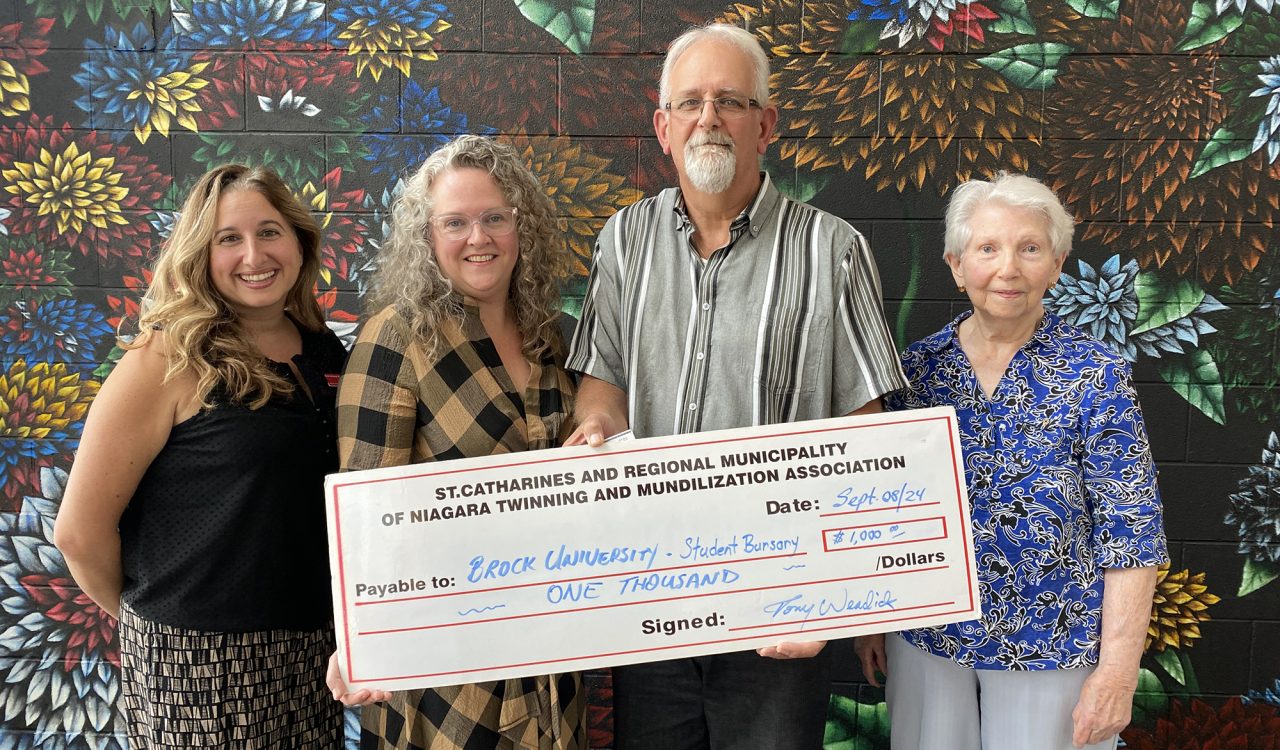 Four people stand together holding a large cheque.