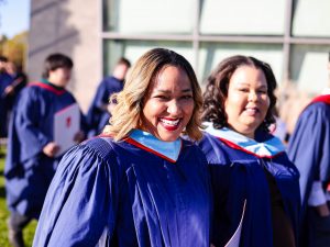 A group of graduates in blue gowns walk together outside.