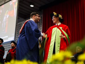 A graduate shakes hands with another individual in a Convocation robe.