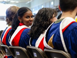 A graduate looks back while sitting in an auditorium with other graduates.