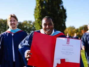 A graduate holds a folder open showing his degree from Brock University.