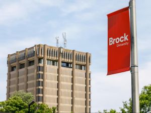 A Brock University banner hands from a pole with a concrete tower in the background.