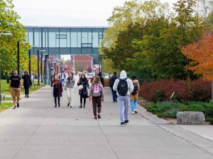 Students walk along an outdoor concrete concourse with a glass walkway overtop.