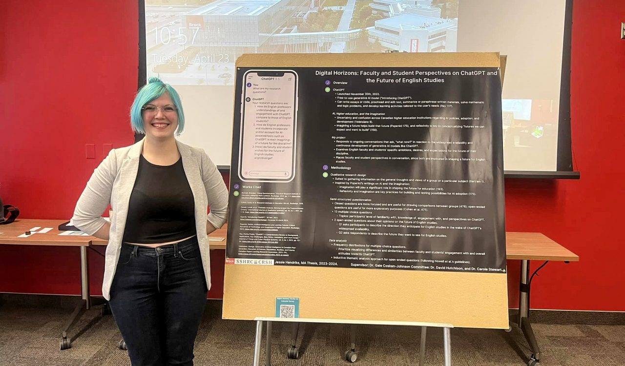 A woman stands in a room with a red wall beside a large poster with text. The woman has dyed bright blue hair and smiles warmly.