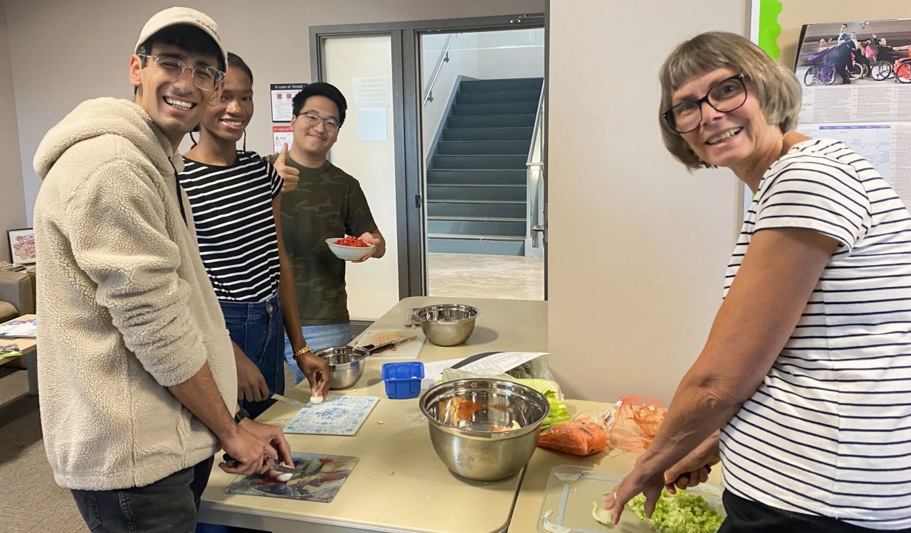 Four people stand around a table preparing a meal.