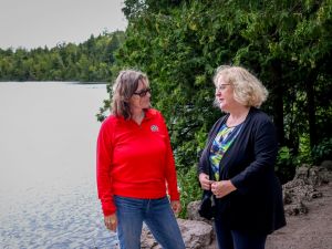 Two women have a conversation beside a lake.