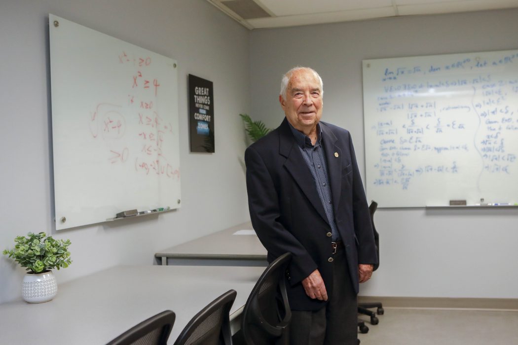 Eric Muller stands in the Eric Muller Mathematics and Statistics Learning Centre at Brock University. Behind him are two whiteboards with math equations on them.