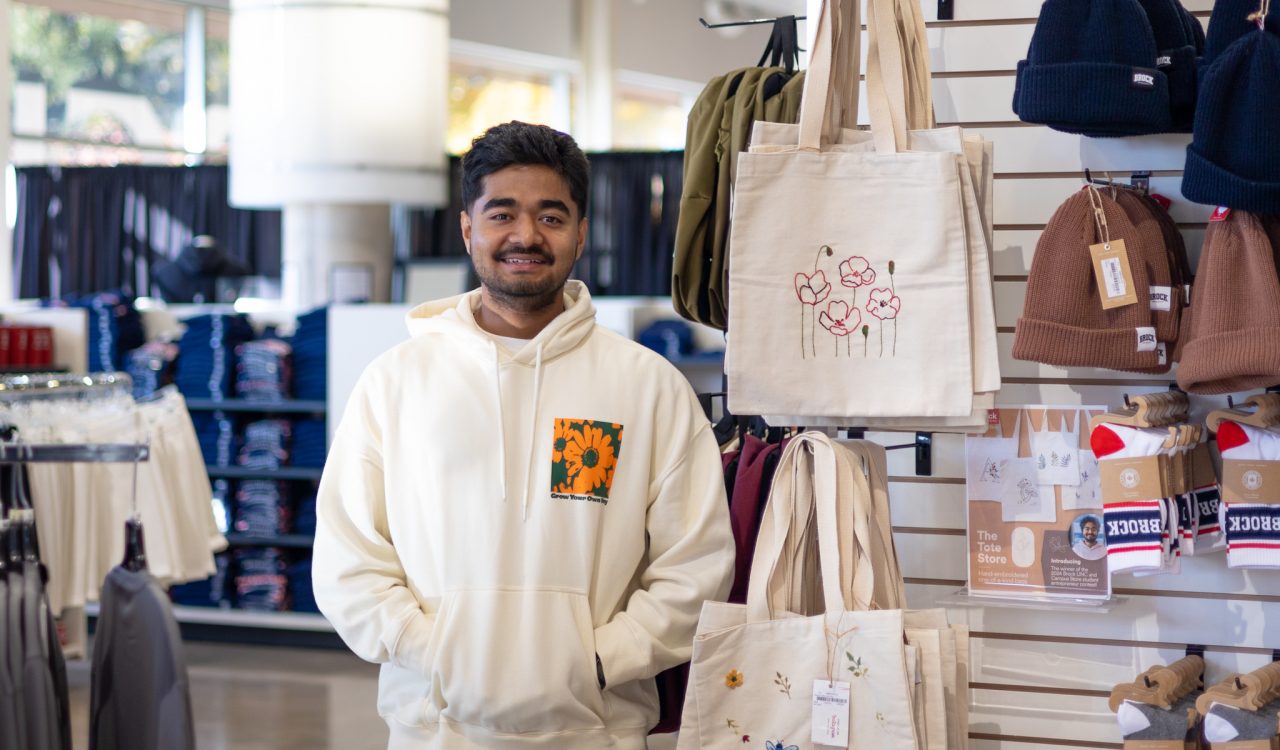 A man stands beside a display of tote bags in a store.