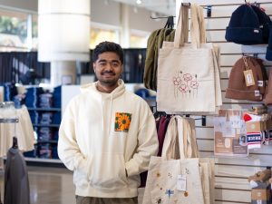 A man stands beside a display of tote bags in a store.