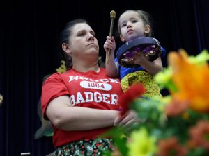 A woman holds a child, who is holding a drum.