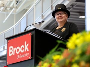 A woman in a top hat stands at a podium with a Brock University sign on it.