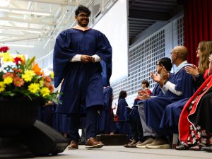 A graduate crosses the Convocation stage while people seated on the stage clap.