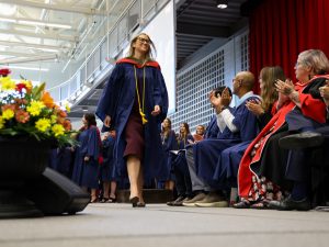 A graduate walks across a Convocation stage while people on the stage clap.