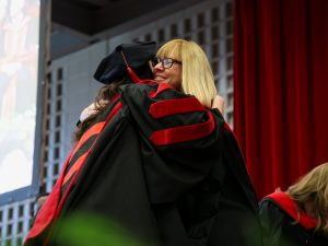 Two women in Convocation gowns hug on stage.