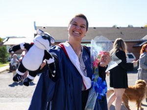 A graduate holds up a stuffed badger toy.